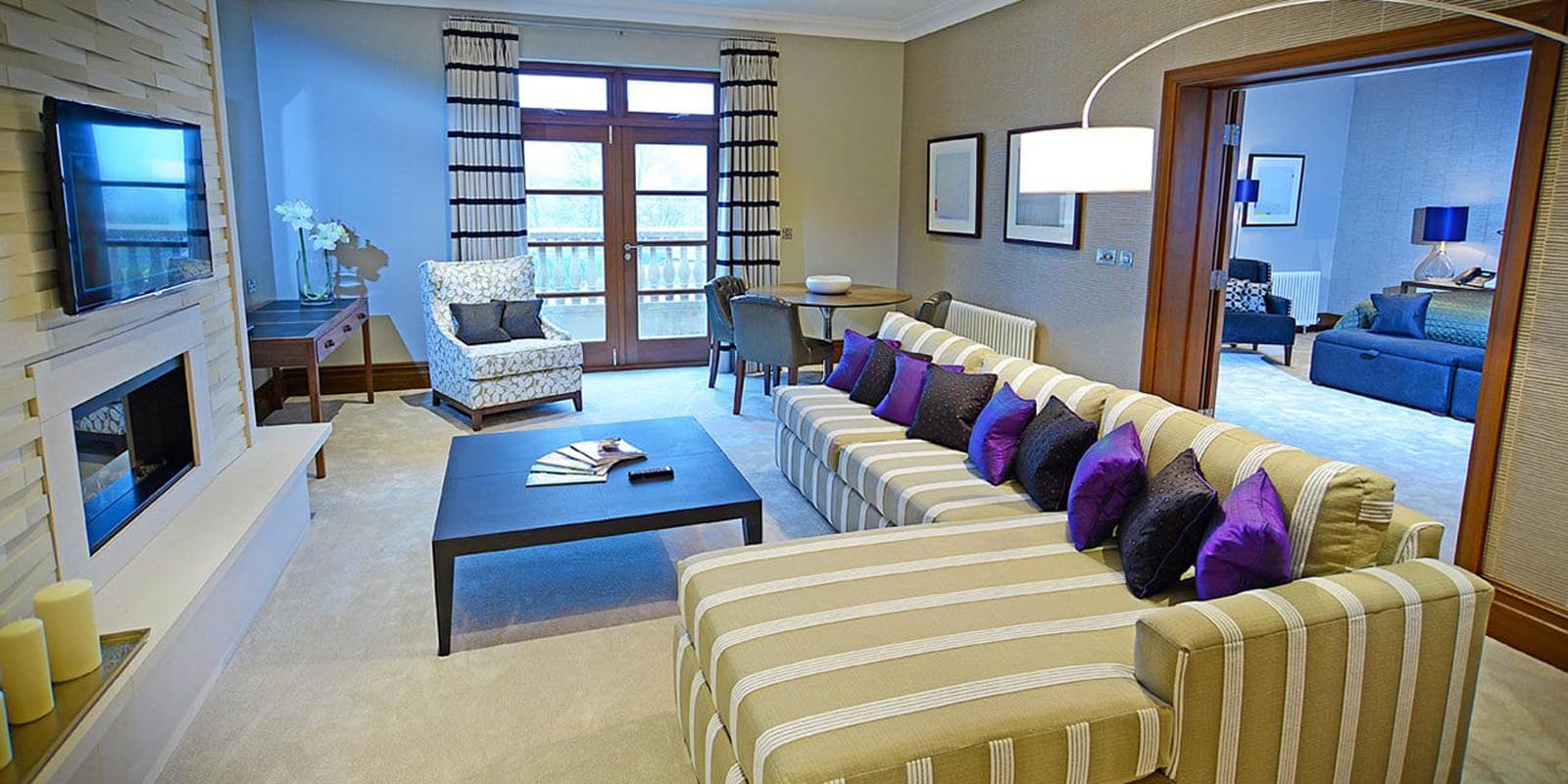 Seating area in the garden lodge suite, with an L shaped sofa, coffee table, TV and fireplace.